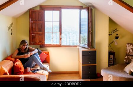 Mature Woman using smart phone while sitting on sofa at home Banque D'Images