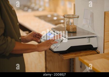 Section médiane de l'entrepreneur féminin pesant le pot de grain sur la balance dans le café Banque D'Images