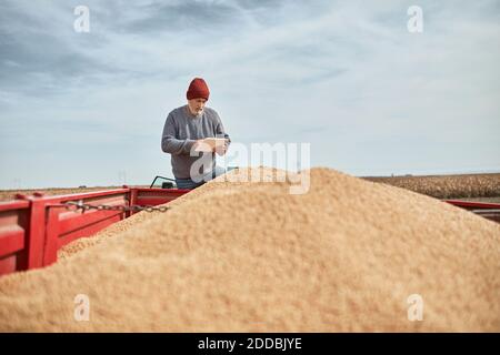 Agriculteur utilisant une tablette numérique tout en se tenant sur le tracteur contre un endroit dégagé ciel Banque D'Images