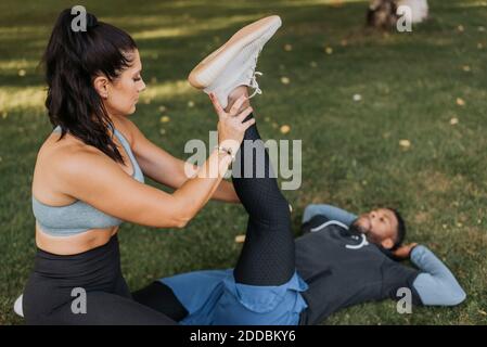 Femme adulte de taille moyenne aidant l'homme tout en étirant ses jambes pendant exercice à l'arrière-cour Banque D'Images
