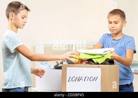 Les enfants bénévoles trient des jouets, des vêtements, des livres, des produits de don dans des boîtes de dons de charité Banque D'Images