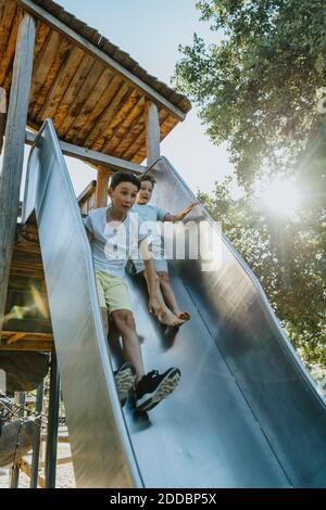 Les frères glissent sur le toboggan dans le parc public par beau temps Banque D'Images