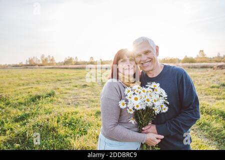 Couple senior heureux tenant des fleurs de camomille sur le terrain ensoleillé jour Banque D'Images