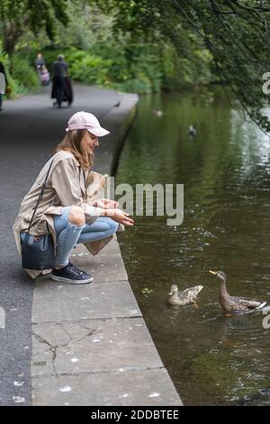 Jeune femme nourrissant un oiseau de colombe dans le lac pendant qu'elle se croupe trottoir Banque D'Images