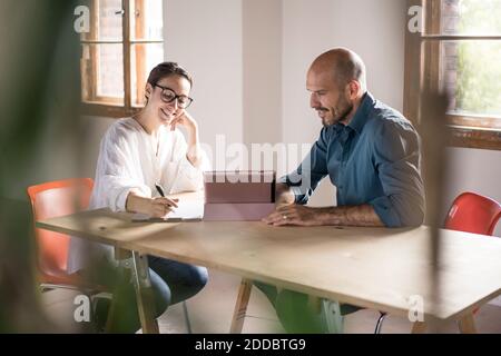 Femme d'affaires écrivant dans le bloc-notes tout en étant assise par l'homme en utilisant le numérique tablette au bureau Banque D'Images