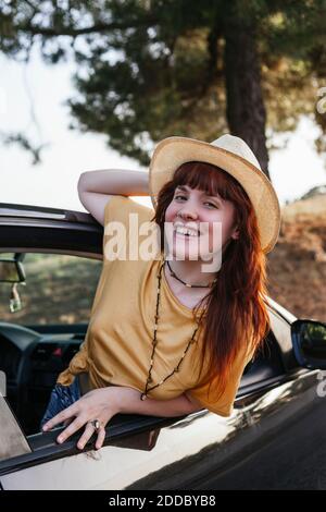 Jeune souriant belle femme rouge s'inclinant de la fenêtre de voiture Banque D'Images