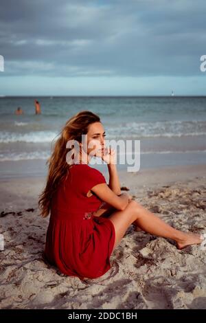 Femme contemplant la vue loin en s'asseyant sur la rive à la plage Banque D'Images