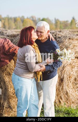 Heureux couple senior baiser en se tenant contre les balles de foin à champ Banque D'Images