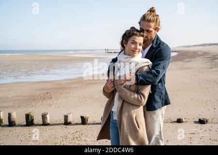 Un jeune couple s'embrasse en se tenant à la plage contre un ciel dégagé Banque D'Images