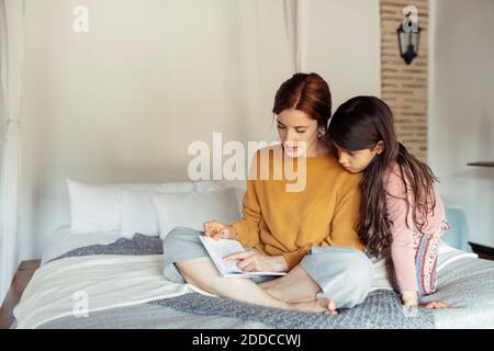 Mère enseignant fille tout en étant assis sur le lit à la maison Banque D'Images