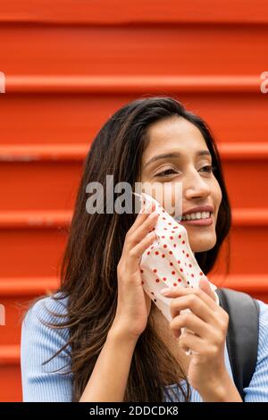 Femme souriante portant un masque de protection tout en se tenant contre l'orange Obturateur pendant COVID-19 Banque D'Images