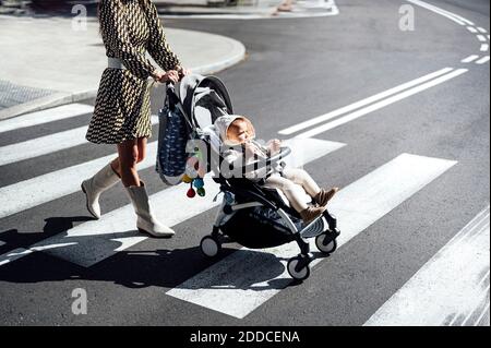 Mère avec bébé garçon dans la rue de traversée de voiture dans la ville par beau temps Banque D'Images