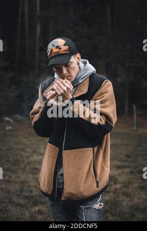 Jeune homme éclairant la cigarette en se tenant dans la forêt pendant l'automne Banque D'Images