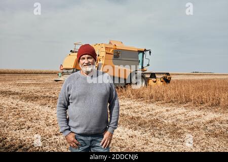 Un fermier souriant se tenant contre un tracteur moissonnant de la récolte à la ferme Banque D'Images