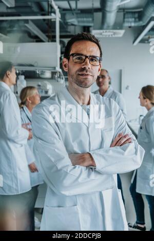 Homme scientifique debout avec les bras croisés et collègue en arrière-plan au laboratoire Banque D'Images