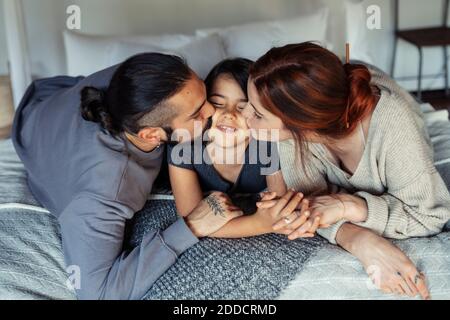 Mère et père embrassant la fille tout en étant allongé sur le lit à accueil Banque D'Images