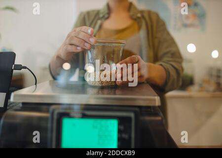 Section centrale de la femme qui pèse le pot à grain sur la balance dans le café Banque D'Images