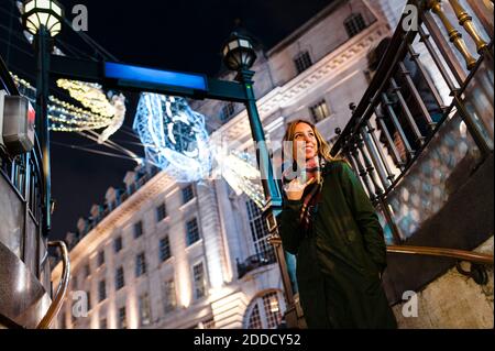 Femme souriante debout sous les lumières de Noël sur Regent Street dans la ville de Londres, Royaume-Uni Banque D'Images