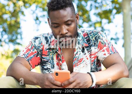 Jeune homme utilisant un smartphone assis à l'extérieur Banque D'Images
