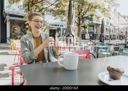 Femme prenant le selfie sur un smartphone en étant assise à l'extérieur café Banque D'Images