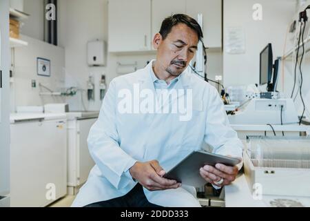 Homme scientifique utilisant une tablette numérique pendant qu'il est assis au laboratoire Banque D'Images