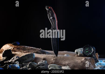 Le revers d'un couteau militaire sur un arbre avec des pierres. Couteau et montre. Banque D'Images