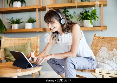Bonne femme mûre utilisant une tablette numérique tout en étant assise à la maison Banque D'Images