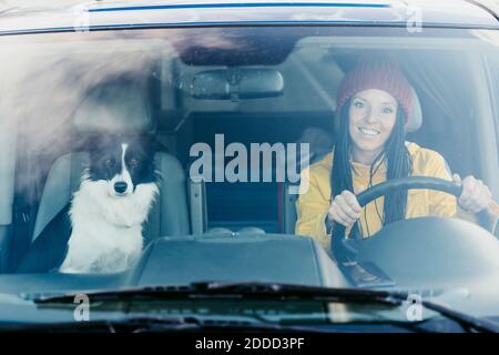 Femme souriante avec chien vu à travers le pare-brise de voiture pendant la route trajet Banque D'Images