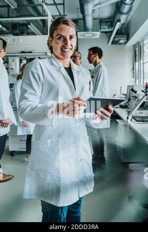 Femme souriante utilisant une tablette numérique tout en étant debout avec un collègue expérience en laboratoire Banque D'Images