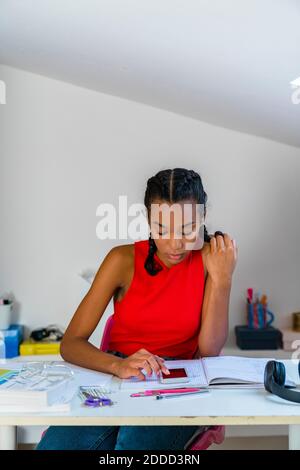 Adolescente utilisant un smartphone tout en étant assise sur une table à accueil Banque D'Images