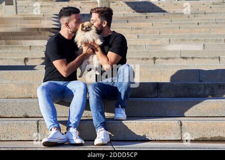 Couple gay embrassant chien en s'asseyant sur des marches à l'extérieur Banque D'Images