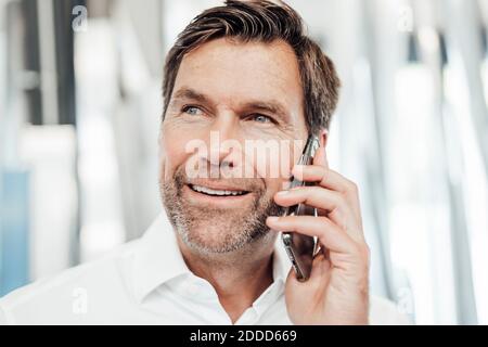 Un homme souriant qui regarde loin tout en parlant sur un smartphone dans l'industrie Banque D'Images