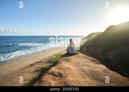 Femme touriste assise sur la formation de roche tout en regardant la mer Banque D'Images