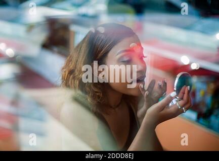 Jeune femme appliquant le rouge à lèvres pendant qu'elle est assise au café Banque D'Images