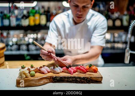 Un chef cuisinier masculin garni de sushi sur un plateau de service en bois dans la cuisine au restaurant Banque D'Images