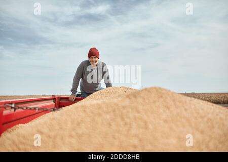 Fermier souriant debout sur le tracteur contre un ciel dégagé Banque D'Images