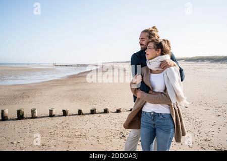 Jeune couple avec les yeux fermés embrassant en se tenant à la plage contre le ciel dégagé Banque D'Images