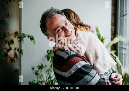 Père souriant tout en portant sa fille dans les bras à la maison Banque D'Images