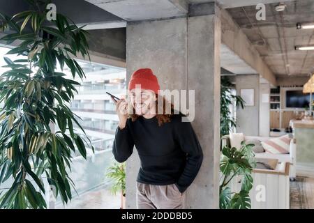 Homme souriant avec mains dans la poche pour écouter du son sur un appareil intelligent téléphone à la maison Banque D'Images