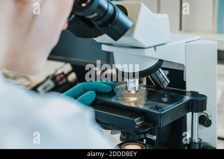 Jeune femme analysant la lame de microscope du cerveau humain sous microscope pendant assis au laboratoire Banque D'Images