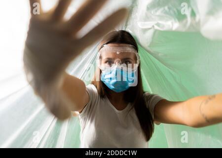 Femme portant un masque facial de protection faisant un geste d'arrêt quand elle est couverte dans le plastique pendant le coronavirus Banque D'Images