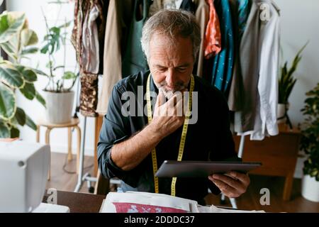 Homme mûr et réfléchi sur mesure tout en regardant la tablette numérique dans studio de travail Banque D'Images