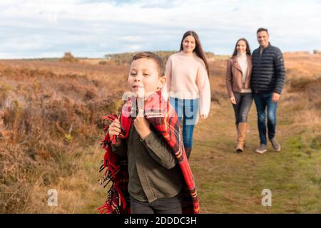 Frère avec foulard courant pendant que les parents et la sœur marche de derrière dans le parc Banque D'Images