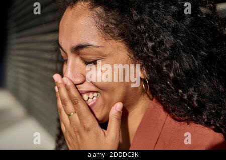 Jeune femme riant avec les yeux fermés contre l'obturateur sous le soleil jour Banque D'Images