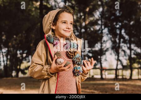 Jolie fille souriante avec guirlande en pin colorée et en forme de cône qui donne sur l'extérieur en vous tenant au parc Banque D'Images