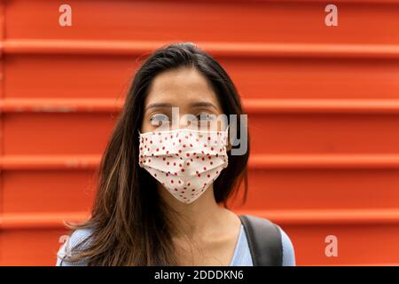 Femme contemplative avec masque de protection debout contre l'obturateur pendant COVID-19 Banque D'Images