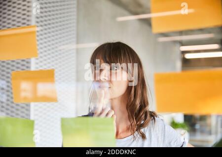 Femme réfléchie avec la main sur le menton regardant des notes collantes Banque D'Images