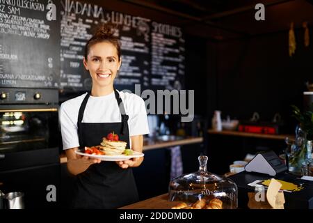 Portrait d'une femme de Barista souriante donnant des crêpes dans l'assiette à café Banque D'Images