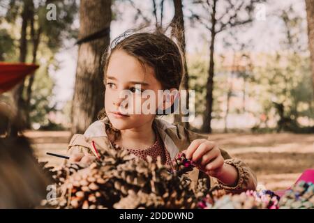 Jolie fille regardant loin tout en colorant le cône de pin au parc Banque D'Images