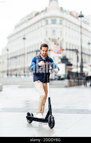 Jeune homme faisant le paiement sans contact de scooter électrique en position debout sur le sentier de la ville Banque D'Images